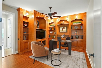 Versatile office, den, or man cave featuring rich custom built-ins, wood flooring, and warm ambient lighting.