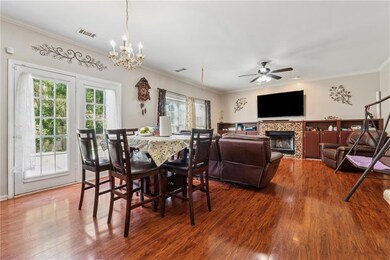 Dining space with wood finished floors, crown molding, a chandelier, a tiled fireplace, and ceiling fan
