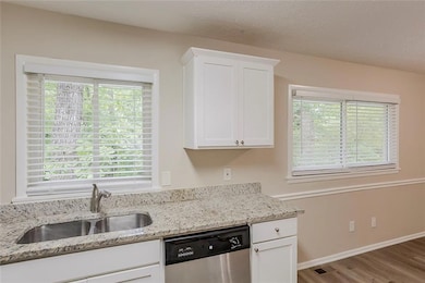 Kitchen featuring dishwasher, a sink, wood finished floors, and white cabinetry
