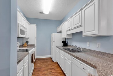 Kitchen with white appliances, a textured ceiling,