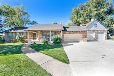 Single story home featuring covered porch, brick siding, a detached garage, a front lawn, and concrete driveway