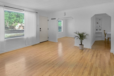 Unfurnished living room featuring arched walkways, light wood-style floors, and crown molding