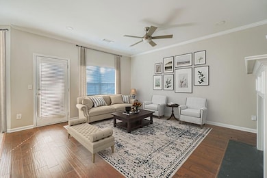Living room featuring crown molding, wood finished floors, ceiling fan, and a fireplace with flush hearth