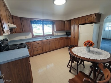Kitchen featuring freestanding refrigerator, black range with electric cooktop, brown cabinets, and light floors