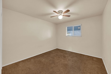 Unfurnished room featuring dark colored carpet and a ceiling fan