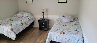 Bedroom with a wainscoted wall, a decorative wall, and wood finished floors