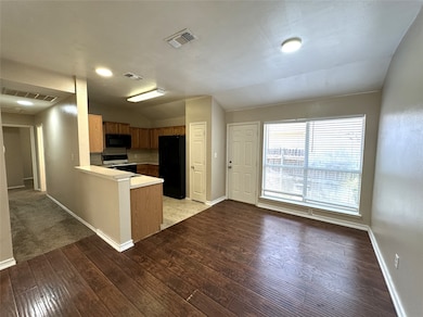 Kitchen with vaulted ceiling, a peninsula, black appliances, light countertops, and light wood-style floors