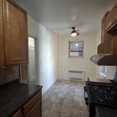 Kitchen with gas stove, ceiling fan, radiator heating unit, dark countertops, and decorative backsplash
