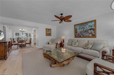 Living room with ceiling fan with notable chandelier, light wood-type flooring, and crown molding
