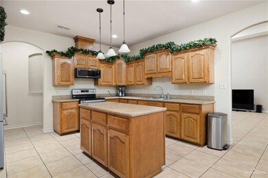 Kitchen featuring hanging light fixtures, sink, light tile patterned floors, appliances with stainless steel finishes, and a kitchen island