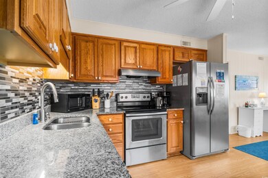Kitchen featuring stainless steel appliances, a sink, under cabinet range hood, decorative backsplash, and a textured ceiling