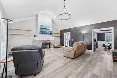Living room with a chandelier, wood finished floors, lofted ceiling, and a brick fireplace