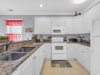 Kitchen with white appliances, white cabinetry, light tile patterned floors, dark stone countertops, and recessed lighting