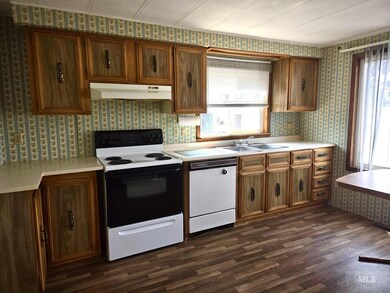 Kitchen with white appliances, under cabinet range hood, wallpapered walls, dark wood-style floors, and light countertops