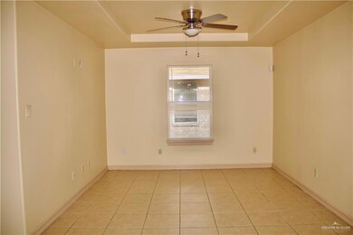 Empty room featuring a tray ceiling, baseboards, light tile patterned floors, and a ceiling fan