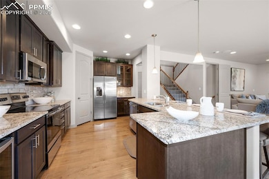 Kitchen with stainless steel appliances, a sink, beverage cooler, decorative backsplash, and light wood-type flooring