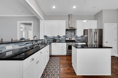 Kitchen featuring appliances with stainless steel finishes, wall chimney exhaust hood, tasteful backsplash, decorative light fixtures, and dark hardwood / wood-style floors