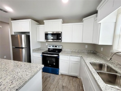 Kitchen featuring stainless steel appliances, light wood-style flooring, white cabinets, and light stone countertops