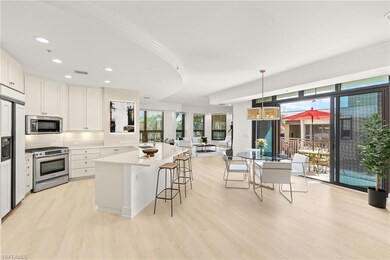 Kitchen with appliances with stainless steel finishes, light wood-style flooring, a kitchen breakfast bar, white cabinets, and hanging light fixtures (Virtually Staged)