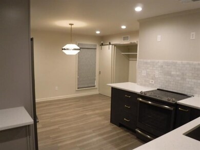 Kitchen with electric stove, a barn door, dark cabinetry, light countertops, and wood finished floors