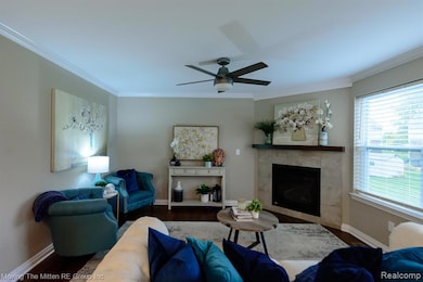 Living room with dark wood-style floors, a fireplace, ornamental molding, and a ceiling fan