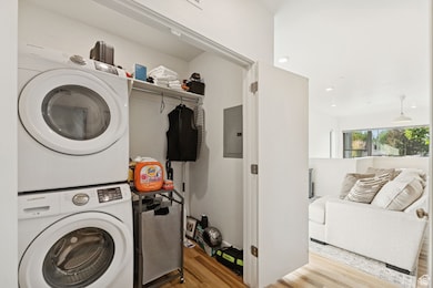 Washroom with light wood-style floors, stacked washing machine and dryer, electric panel, and recessed lighting