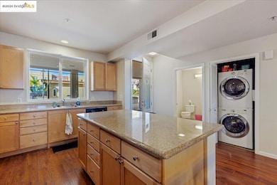 Kitchen featuring light brown cabinetry, estacked washer and dryer, a kitchen island, light stone countertops, and dark wood-style flooring