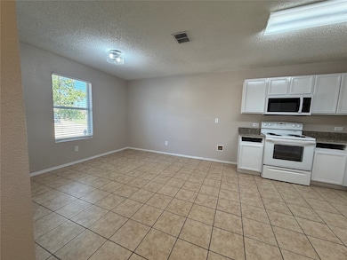 Kitchen with white cabinets, white appliances, light tile patterned flooring, and a textured ceiling