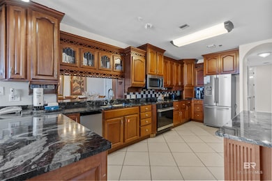 Kitchen featuring light tile patterned flooring, brown cabinets, dark stone counters, stainless steel appliances, and arched walkways
