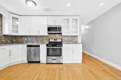 Kitchen featuring light countertops, stainless steel appliances, baseboards, decorative backsplash, and light wood finished floors