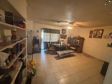 Living area featuring a textured ceiling, light tile patterned flooring, and ceiling fan