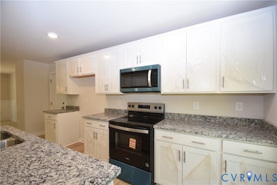 Kitchen with electric range oven, stainless steel microwave, light stone counters, white cabinetry, and recessed lighting