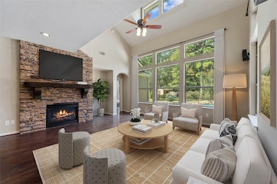 Stunning living room featuring a stacked stone fireplace, soaring ceilings, and rich flooring. A wall of windows fills the space with natural light, creating a warm and inviting atmosphere. Virtually staged.