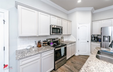 Kitchen featuring tasteful backsplash, appliances with stainless steel finishes, ornamental molding, dark wood-style flooring, and white cabinets