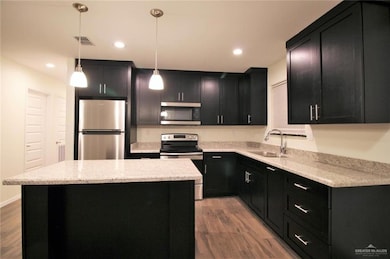 Kitchen featuring dark cabinets, stainless steel appliances, light stone countertops, a kitchen island, and recessed lighting