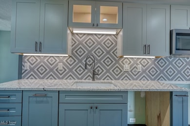 Kitchen featuring stainless steel microwave, light stone countertops, decorative backsplash, and glass insert cabinets