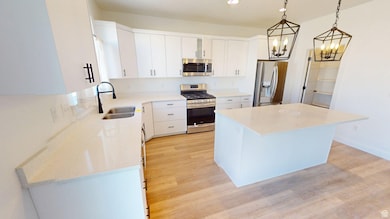 Kitchen featuring stainless steel appliances, pendant lighting, white cabinets, light stone counters, and a kitchen island