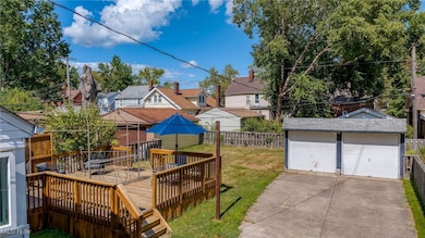 Fenced backyard with a deck, a residential view, a detached garage, and an outbuilding