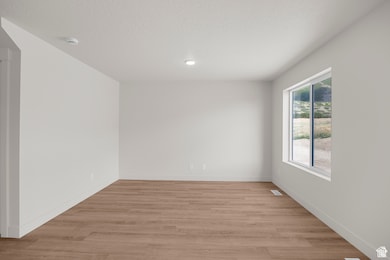 Spare room with light wood-type flooring, a textured ceiling, and recessed lighting