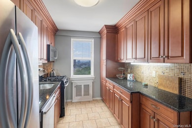 Kitchen featuring appliances with stainless steel finishes, tasteful backsplash, dark stone countertops, and brown cabinets