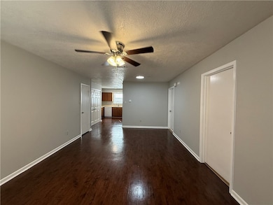 Unfurnished living room with a textured ceiling, dark wood-type flooring, and a ceiling fan