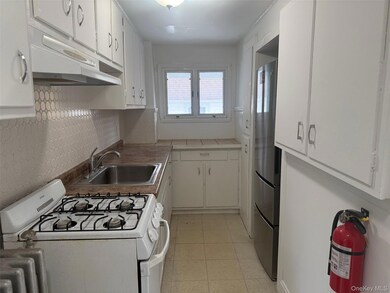 Kitchen with white gas range oven, white cabinets, under cabinet range hood, freestanding refrigerator, and light tile patterned flooring