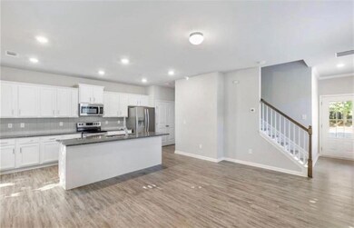 Kitchen with tasteful backsplash, white cabinetry, an island with sink, stainless steel appliances, and light wood-style floors