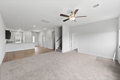 Unfurnished living room featuring light colored carpet, a ceiling fan, light wood-style flooring, recessed lighting, and stairway