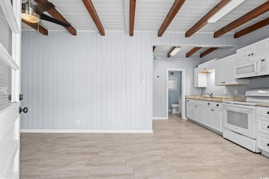 Kitchen featuring white appliances, white cabinets, light stone counters, wooden walls, and beamed ceiling