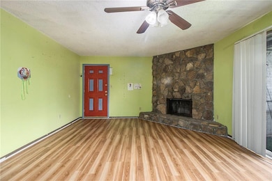 Unfurnished living room featuring a textured ceiling, wood finished floors, a stone fireplace, and ceiling fan