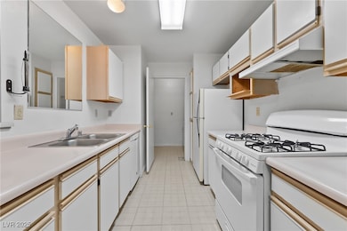 Kitchen featuring white gas range oven, under cabinet range hood, light countertops, and light tile patterned floors