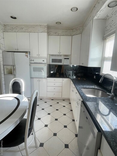 Kitchen with white cabinetry, white appliances, and dark stone counters