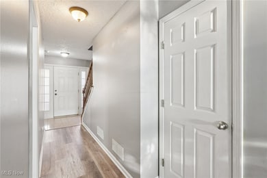 Hallway with stairway, light wood-style flooring, and a textured ceiling