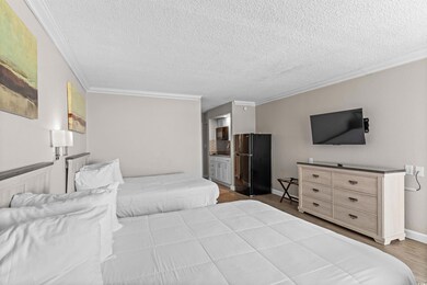 Bedroom with crown molding, light wood-style floors, freestanding refrigerator, and a textured ceiling